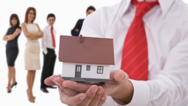 Businesspeople shaking hands and posing with dummy of house